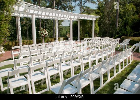 White rental chairs are set in rows behind a pergola awaiting an outdoor summer wedding Stock Photo