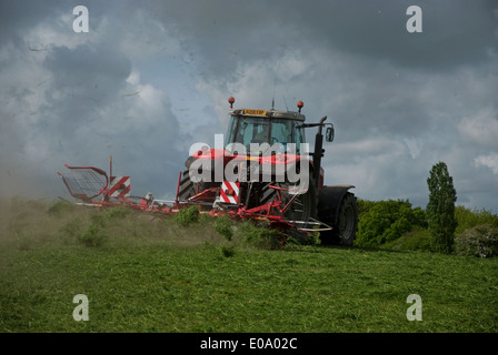 Tractor turning grass to dry for silage in British countryside in spring Stock Photo