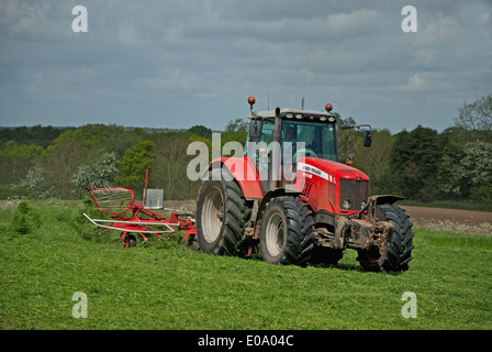 Tractor turning grass to dry for silage in British countryside in spring Stock Photo