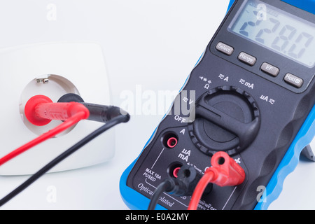 The image shows a plug socket and a multimeter, isolated on white ...