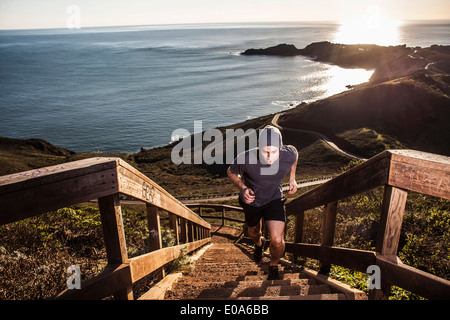 Young man running up coastal staircase at sunset Stock Photo