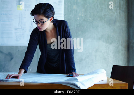 Businesswoman studying blueprints in office Stock Photo