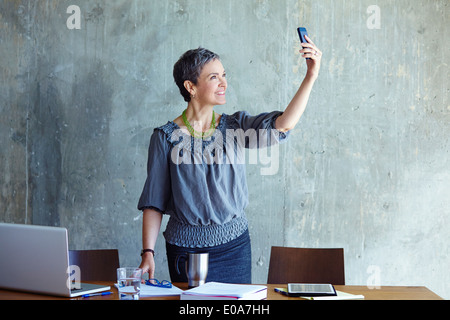 Mature businesswoman taking self portrait in office Stock Photo
