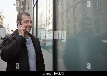 Mid adult man talking on smartphone while window shopping Stock Photo