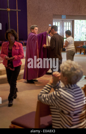 The robed priest of a Catholic church in Laguna Niguel, CA, performs the sacrament of anointing the sick as a parishioner prays in the foreground. Stock Photo