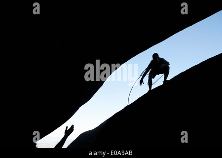 Silhouette of young male climbers reaching out for each other on rock Stock Photo