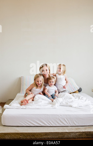 Portrait of mid adult woman in bed with three daughters