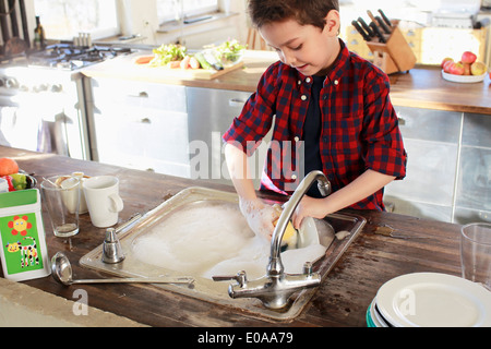 Young boy washing up in kitchen Stock Photo
