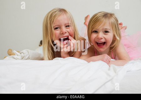 Portrait of two young sisters lying on front in bed Stock Photo