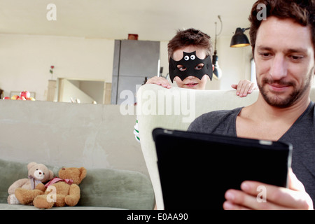 Masked son distracting father from digital tablet Stock Photo