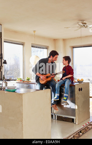 Father and young son playing guitar in kitchen Stock Photo