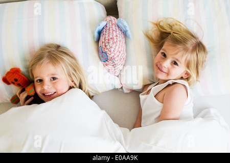 Portrait of two young sisters lying side by side in bed