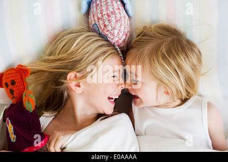 Portrait of two young sisters lying face to face in bed Stock Photo