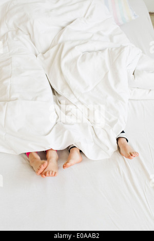 Young sisters feet sticking out of duvet on bed