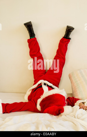 Young boy dressed up as santa claus on bed with legs raised Stock Photo