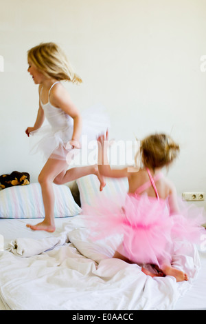 Sisters dressed as ballet dancers running on bed Stock Photo