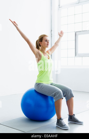 Young woman sitting on exercise ball, arms raised