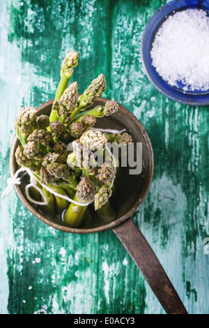 Bunch of young green asparagus in vintage pot over green wooden table. Top view. Stock Photo