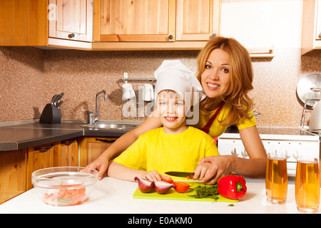 Happy boy using toque cuts vegetables with mother Stock Photo