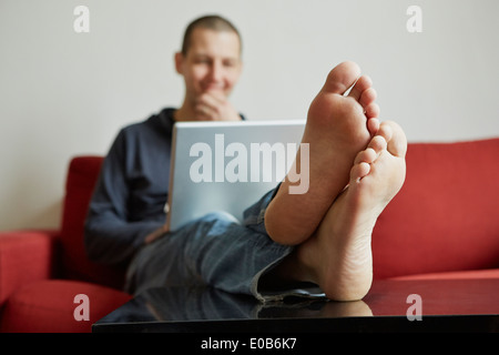 Mid adult man relaxing on sofa engrossed in laptop Stock Photo