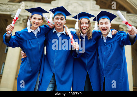 Group of smart students in graduation gowns with diplomas shouting excitedly Stock Photo
