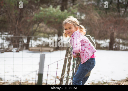 Young girl climbing wire fence in field Stock Photo