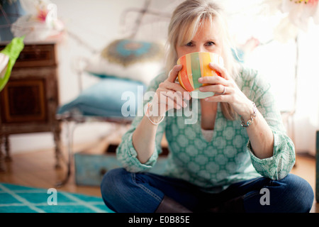 Mature woman sitting cross legged drinking coffee Stock Photo
