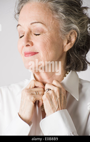 Portrait of senior woman, hands on collar, eyes closed
