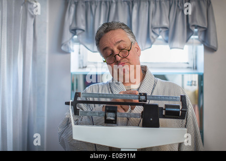 Unhappy mature man on bathroom weighing scales Stock Photo