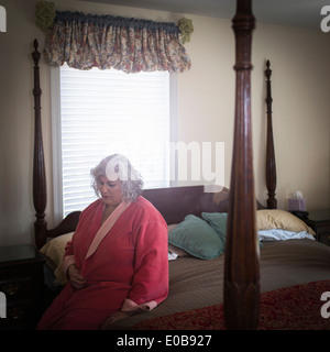 Unhappy mature woman sitting on bed Stock Photo