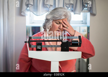 Unhappy mature woman on bathroom weighing scales Stock Photo