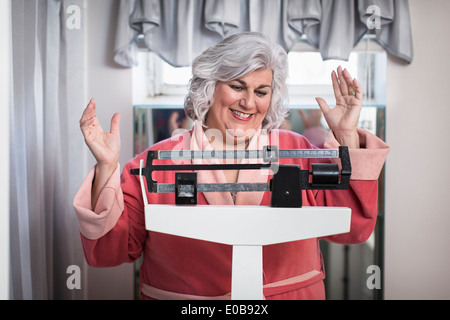 Happy mature woman on bathroom weighing scales Stock Photo