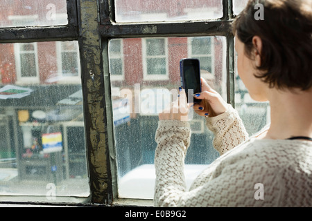 Young woman photographing street below from window Stock Photo