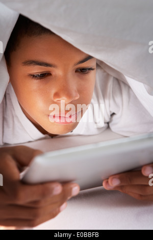 Boy Using Digital Tablet Under Duvet Stock Photo