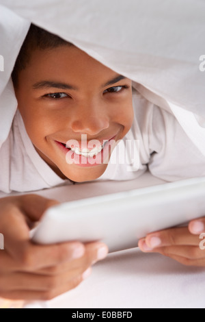 Boy Using Digital Tablet Under Duvet Stock Photo
