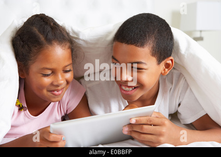 Two Children Using Digital Tablet Under Duvet Stock Photo