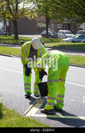 Two workman painting zig-zag yellow lines on newly tarmaced road. Stock Photo