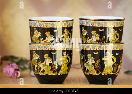 The beautiful tea cups decorated with a list with gold with the image of scenes from antique life. Stock Photo