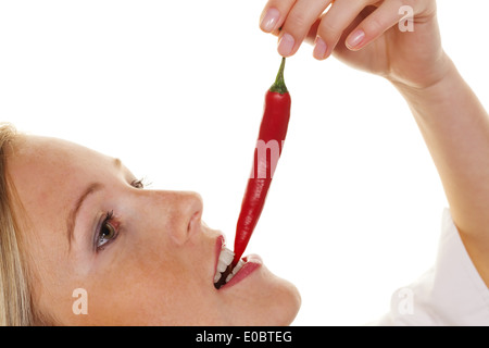 A young woman bites in a Chilli pod. Before white background, Eine junge Frau beisst in eine Chilli Schote. Vor weissem Hintergr Stock Photo