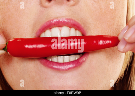 A young woman bites in a Chilli pod. Before white background, Eine junge Frau beisst in eine Chilli Schote. Vor weissem Hintergr Stock Photo