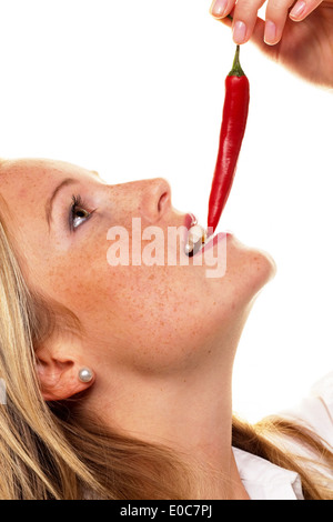 A young woman bites in a Chilli pod. Before white background, Eine junge Frau beisst in eine Chilli Schote. Vor weissem Hintergr Stock Photo