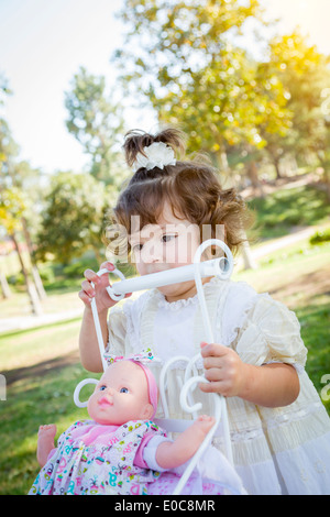 Adorable Young Baby Girl Playing with Her Baby Doll and Carriage Outdoors. Stock Photo