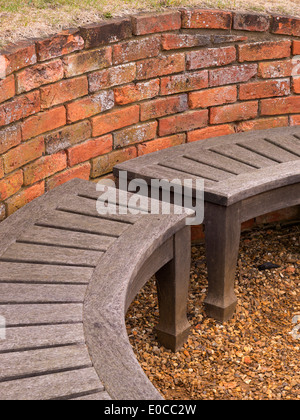 Curved wooden bench seat and old red brick wall, Coton Manor Gardens, Coton, Northamptonshire, England, UK Stock Photo