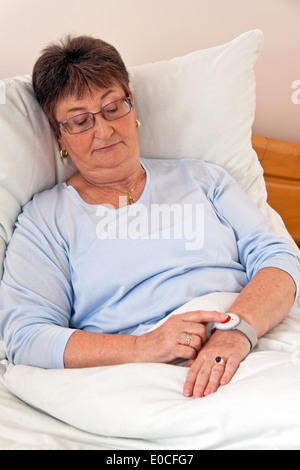 a senior with call help emergency phone in the bed, eine Seniorin mit Ruf Hilfe Notfall Telefon im Bett