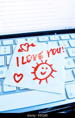 A note slip of paper lies on the keyboard of a computer in memory: I love you Stock Photo