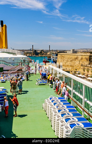 Passengers, bathed in brilliant sunshine, watch from the sun deck of the luxury cruise ship Aurora as it sails into Valletta Stock Photo