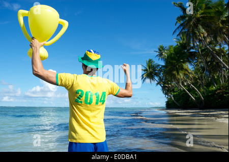 Brazilian football player in 2014 shirt Brazil colors holding trophy up on remote beach in Nordeste Bahia Stock Photo