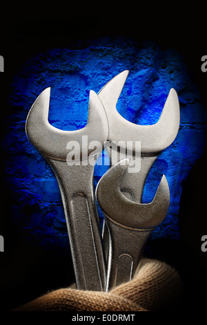 Metallic wrenches in male hand on wall background Stock Photo