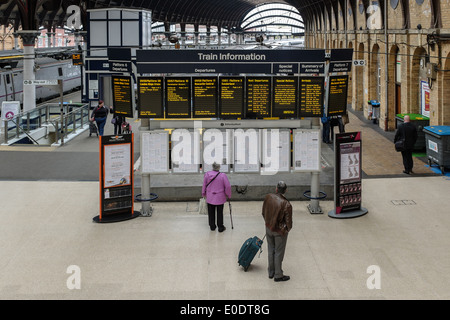 Two older adults check train times on dot matrix displays and printed timetables at York Station, England Britain Yorkshire UK. Stock Photo