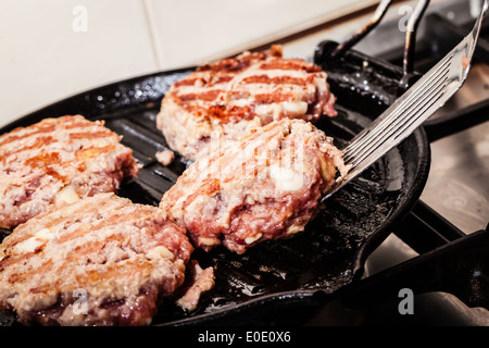 four homemade hamburgers being flipped with a spatula on a pan Stock Photo